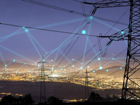 Power distribution lines and towers over cityscape at night with interconnected dots for blog on Cyber Safety in Energy Sector