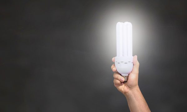 A hand holding up a lit LED bulb